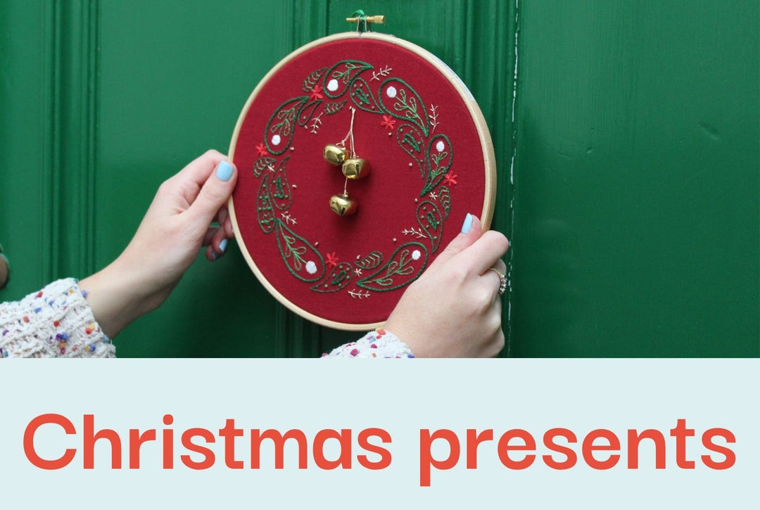 A photo of two hands holding an embroidered Christmas wreath on red fabric against a green painted door.