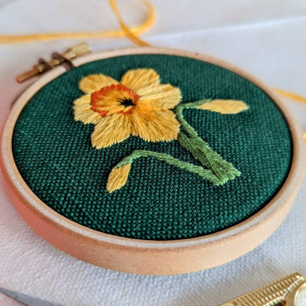 A close up photo a a yellow daffodil embroidered on a green fabric
