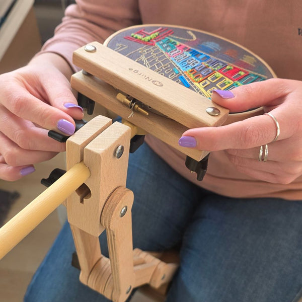 Person using a wooden embroidery hoop stand with colorful fabric inside.