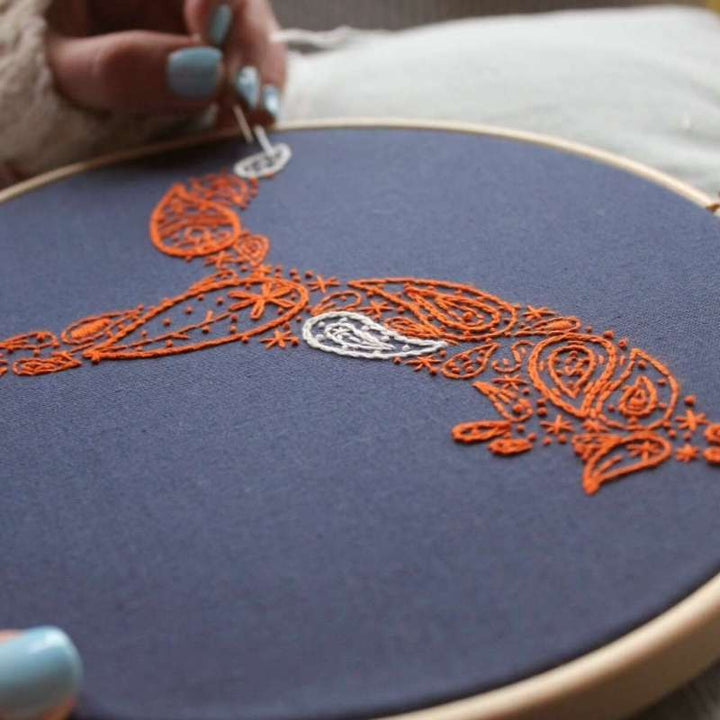 Embroidered orange fox with white flourishes being sewn on navy fabric