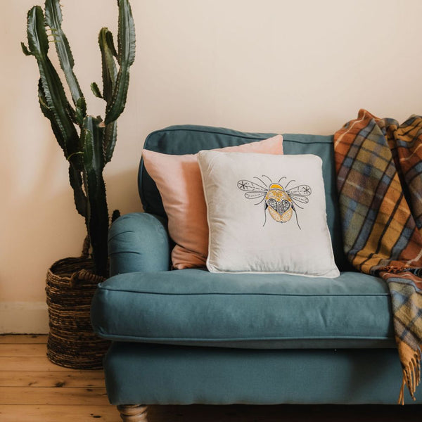 A Paraffle Bee cushion shown finished and sat on a green sofa