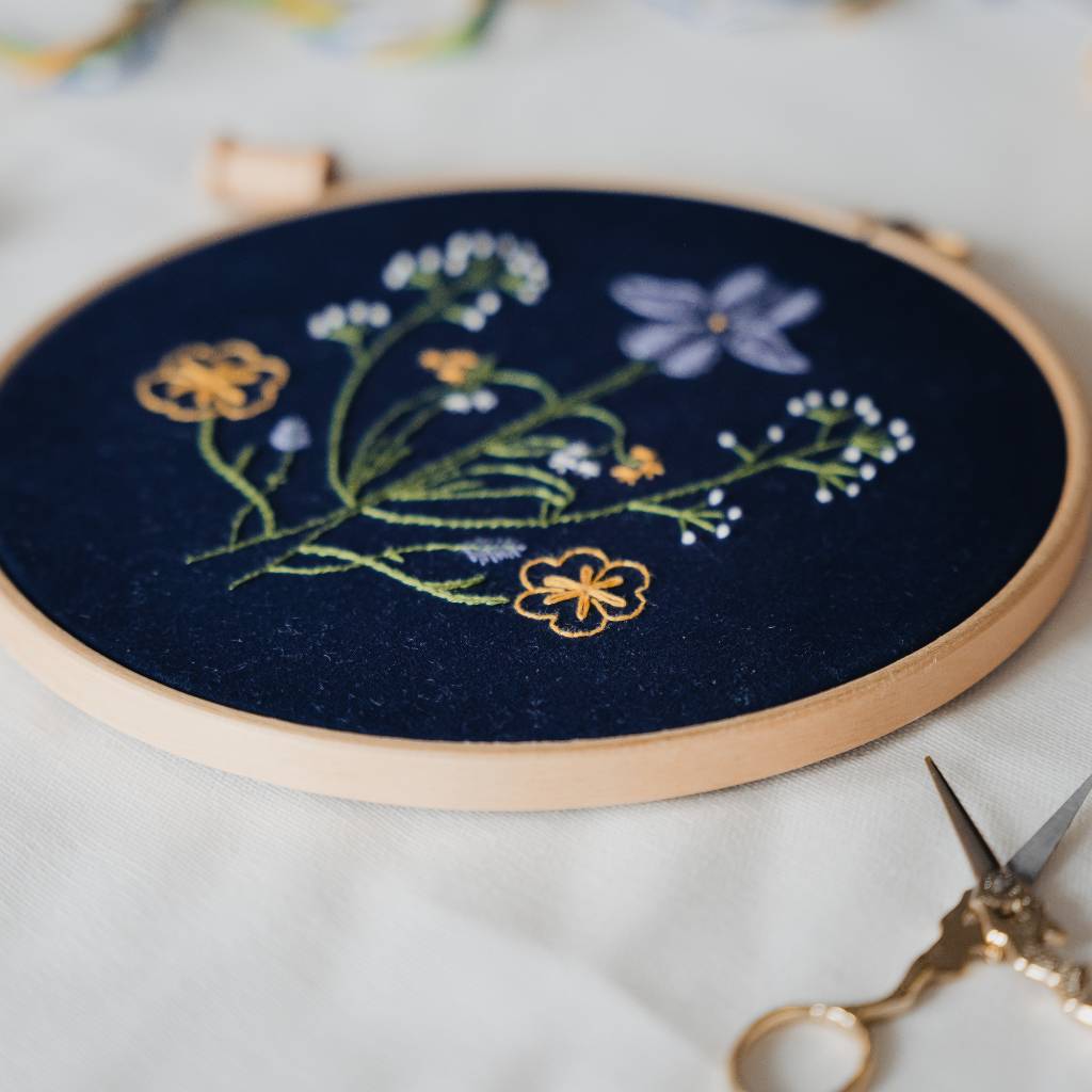 A finished Botanicals embroidery design on navy fabric, shown at an angle, with decorative scissors in the foreground. Made using this Botanicals Embroidery kit product.