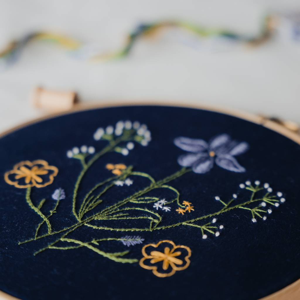A finished Botanicals embroidery design on navy fabric, shown close up at an angle, with decorative supplies in the background. Made using this Botanicals Embroidery kit product.