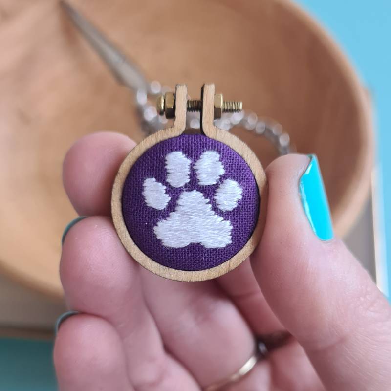 A cats pawprint stitched into purple fabric