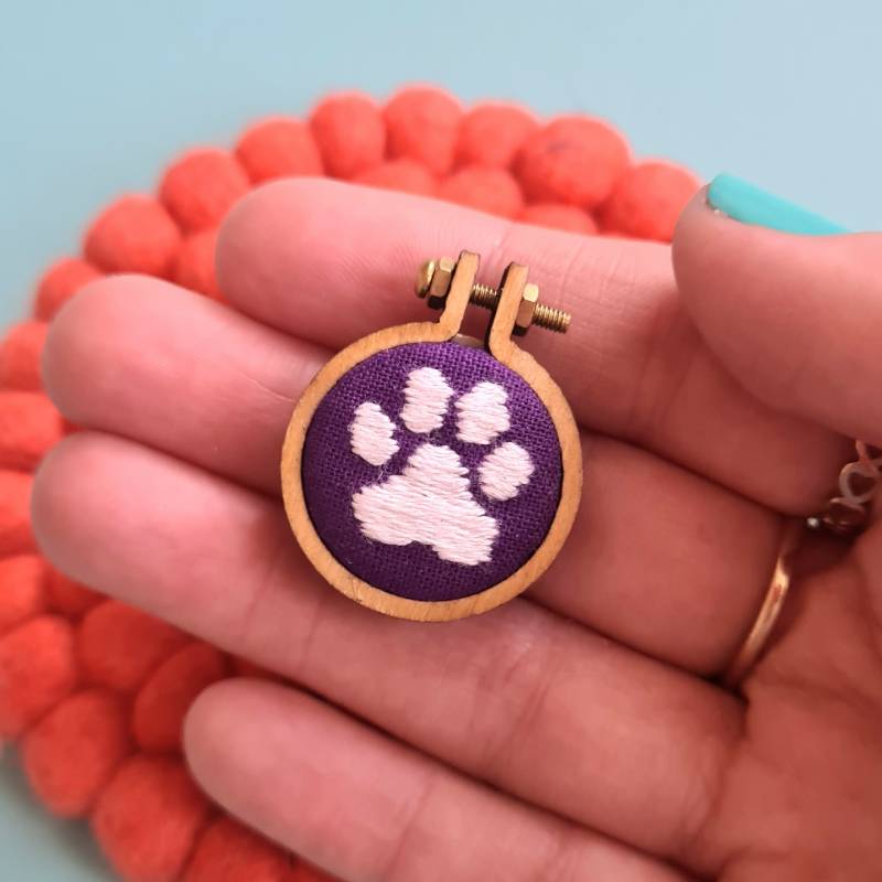 A cats pawprint stitched into purple fabric in a charm