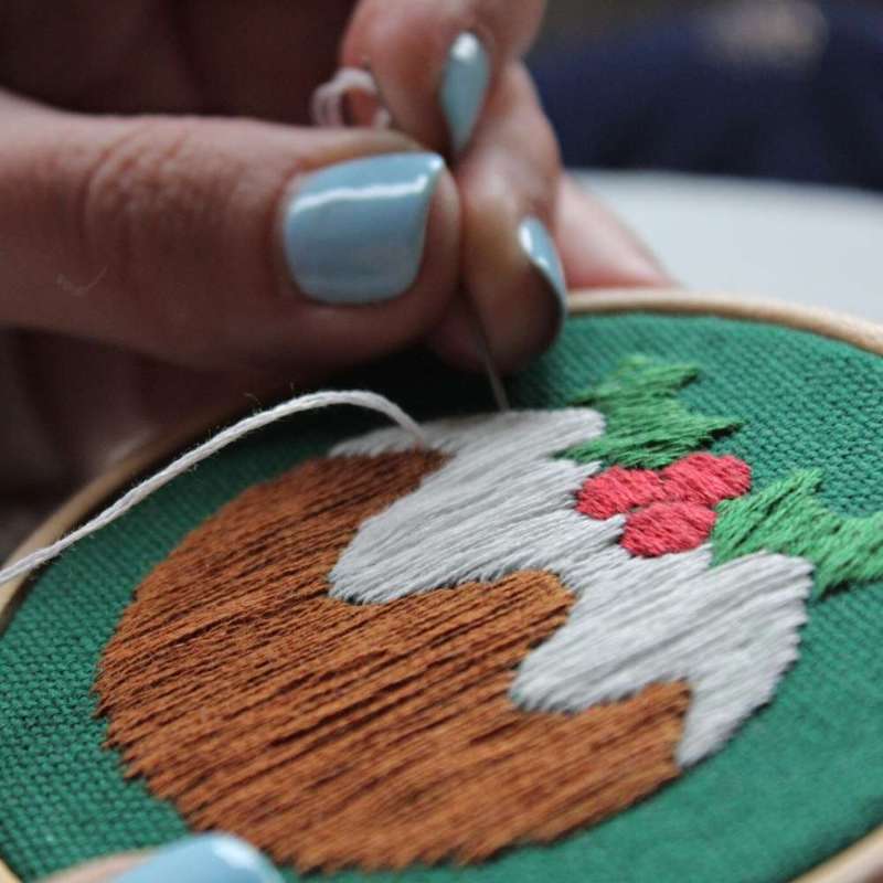 Angled close up photo of a christmas pudding embroidery design being stitched on green fabric