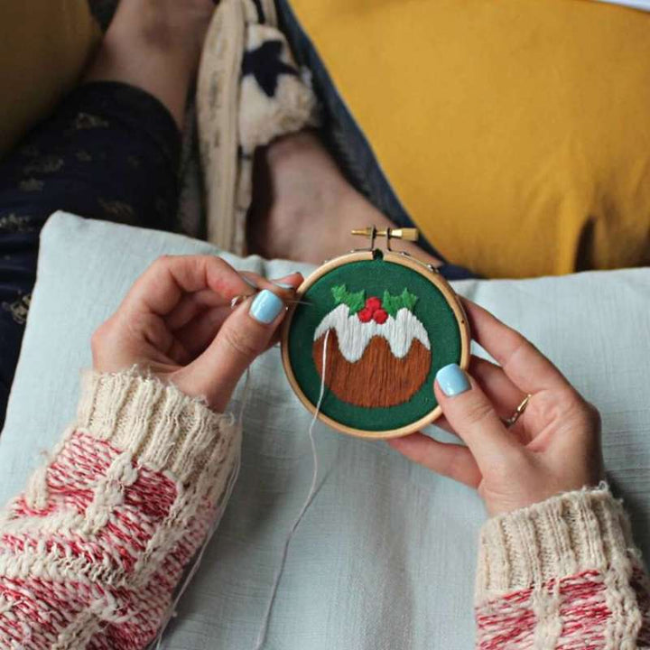 Christmas pudding embroidery bauble held in hands on sofa