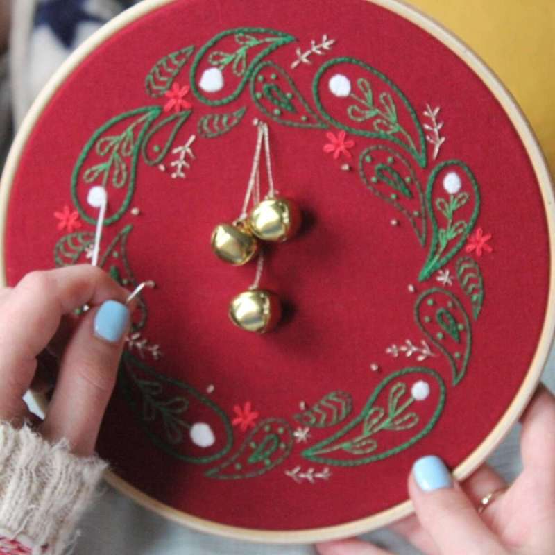 Embroidered christmas wreath held in hands with green door in background