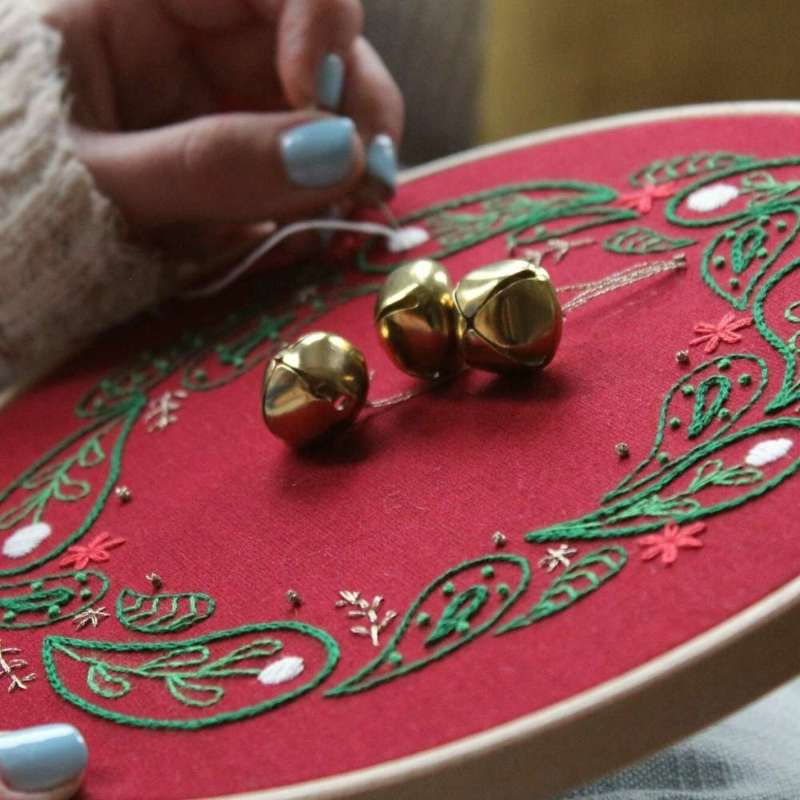 Angled close up shot of embroidered christmas wreath being sewn with bells in the middle