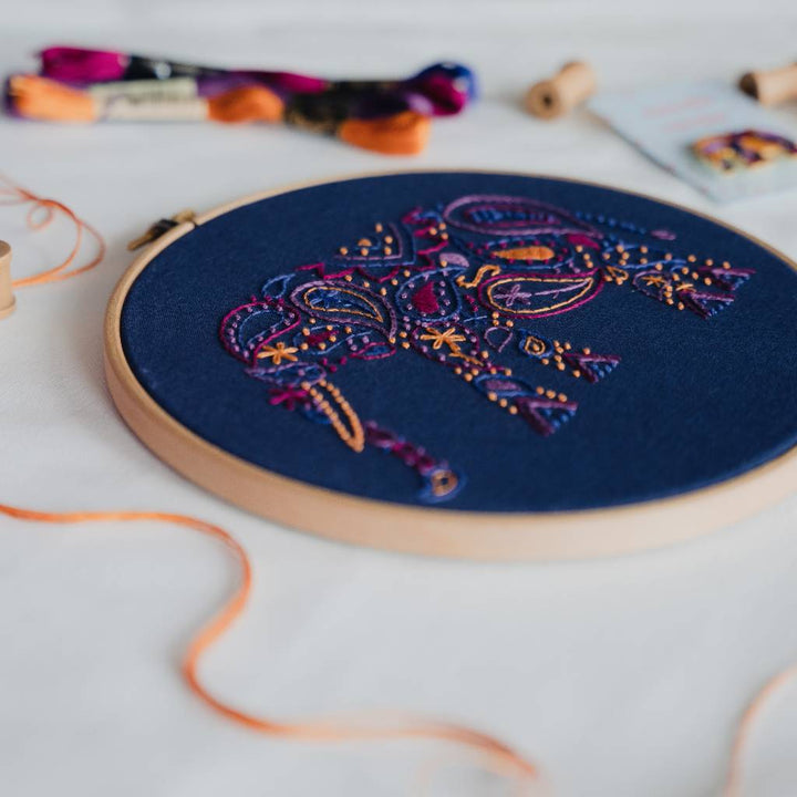 An angled photo of a finished elephant embroidery kit, with thread in the foreground, and a needle minder and thread in the background. Made using this elephant embroidery kit product.