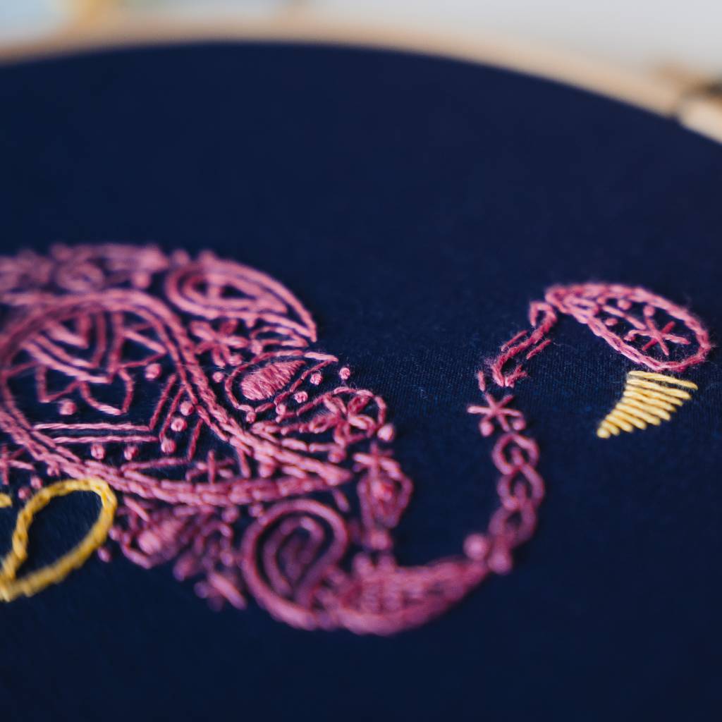 A finished flamingo embroidery design on navy fabric with pink thread and a flamingo needle minder above it and scissors below it. Made using this flamingo embroidery kit product.