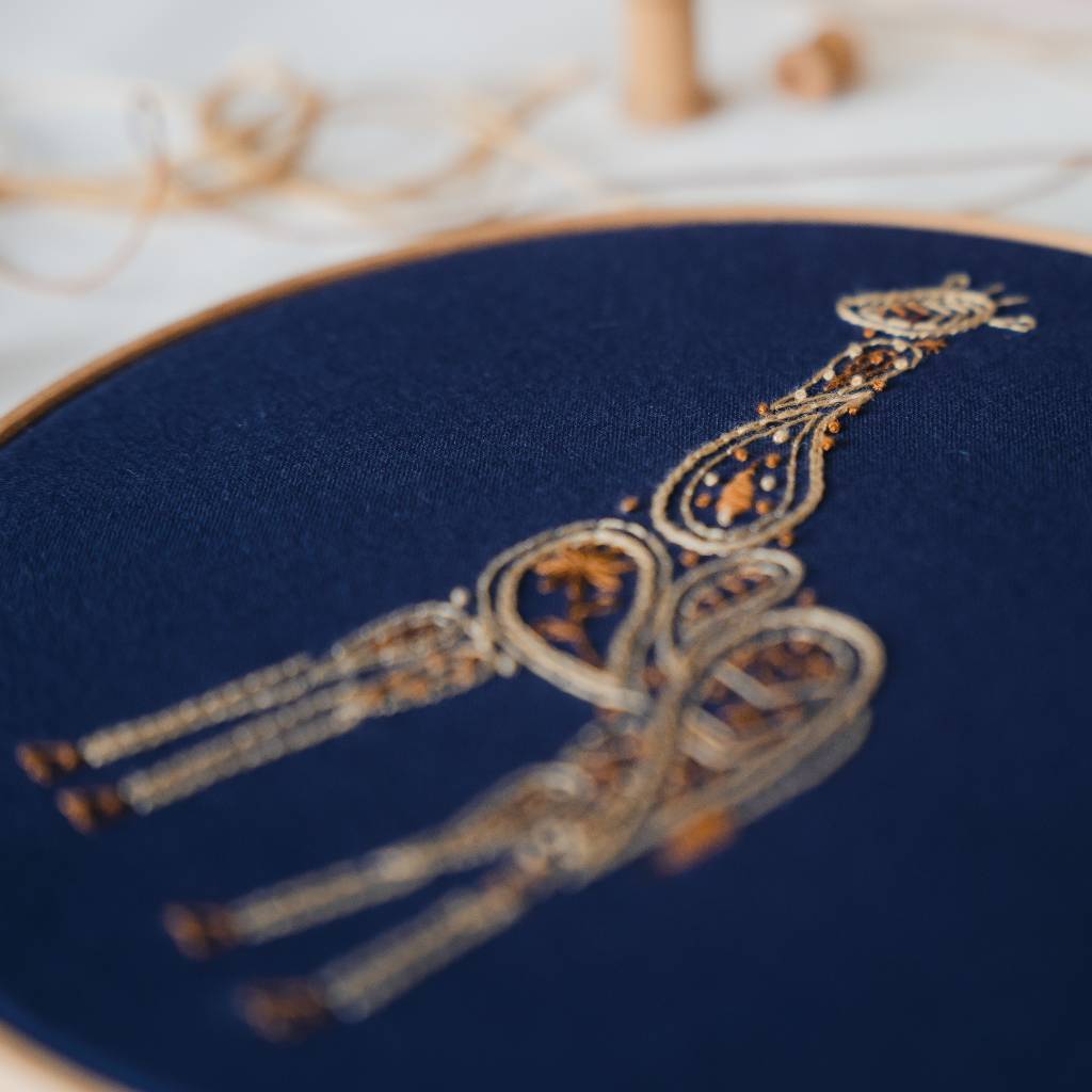 An Angled photo of a finished giraffe embroidery design on navy fabric, with thread in the background. Made using this Giraffe embroidery kit product.
