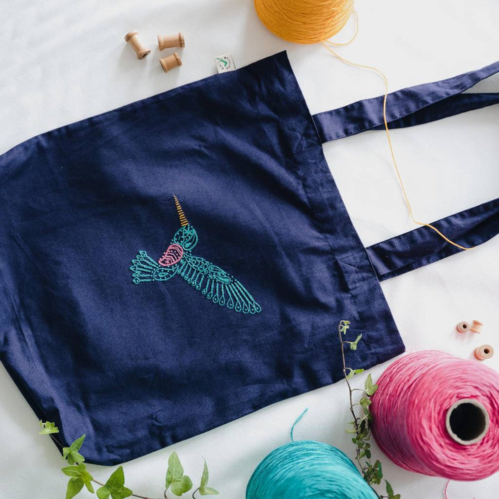 A finished hummingbird embroidery design embroidered on an organic earth positive navy totebag with thread surrounding it. Made using this hummingbird tote bag embroidery kit product.