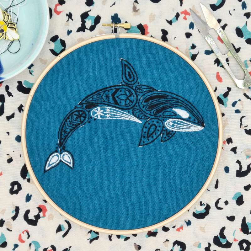 A Black and white embroidered orca on teal fabric and decorations in the background