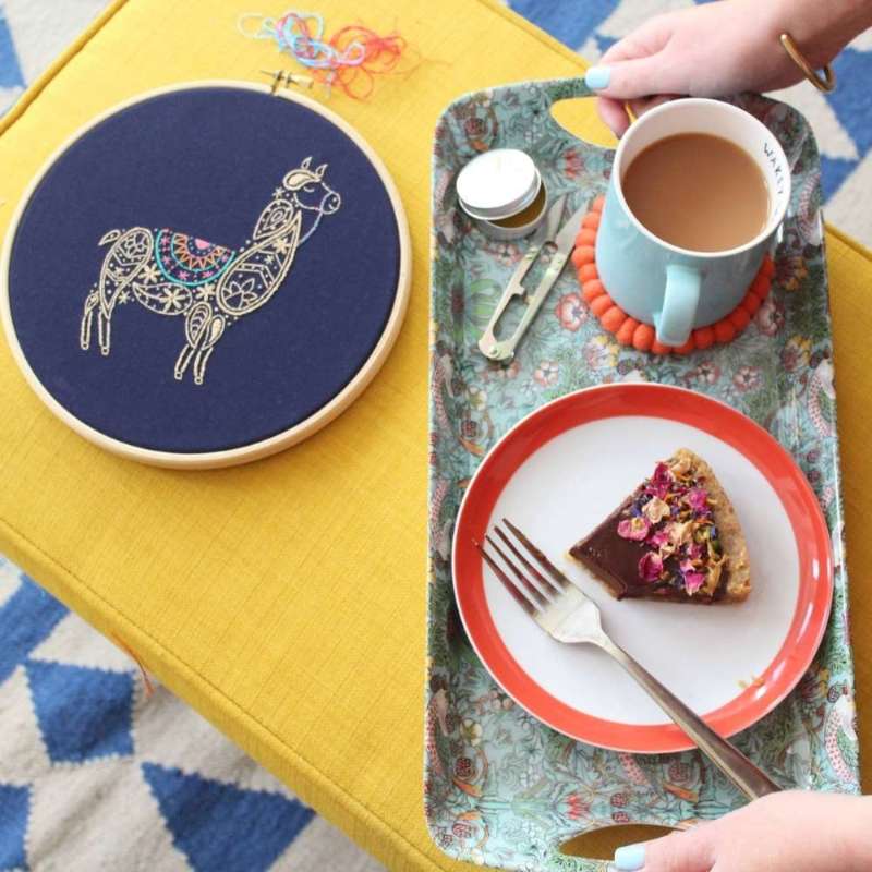 A paisley llama embroidery design in wooden hoop on navy fabric with cake tray next to it