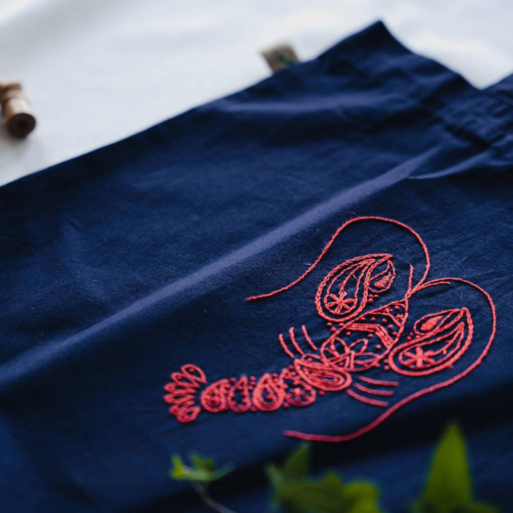 An Angled closeup of a finished lobster embroidery design on an organic navy totebag. Made using this Lobster tote bag embroidery kit.