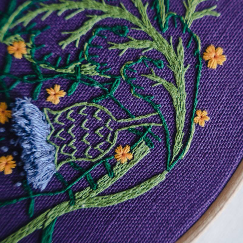 A close up shot of floral embroidery on a dark purple fabric.