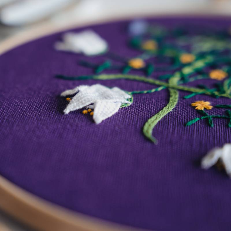 A close up of embroidered white flowers on a deep purple fabric.