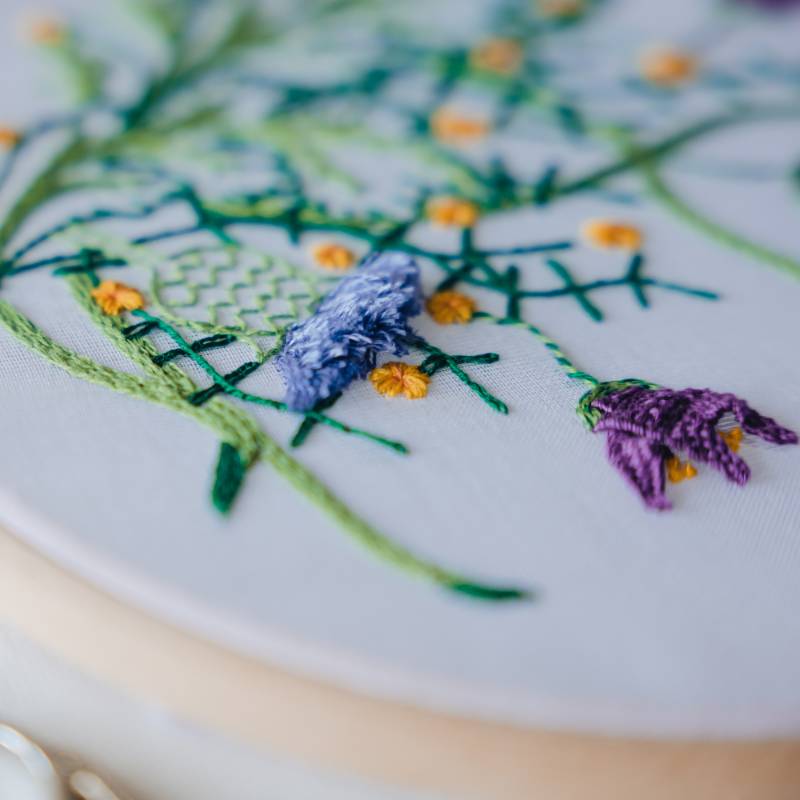A close up of floral embroidery in purple and green thread, on a white fabric.