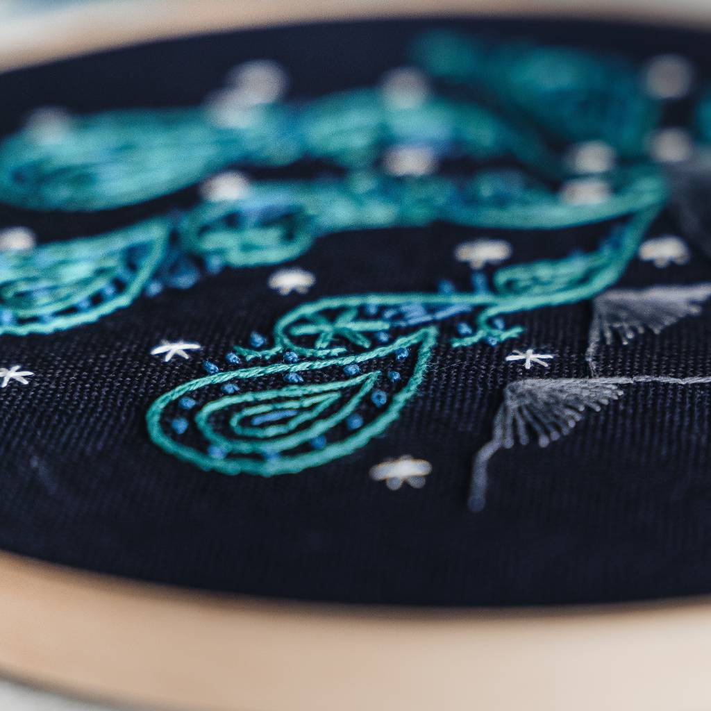 A finished northern lights embroidery design on organic navy fabric, with scissors and thread surrounding it. Made using this northern lights embroidery kit product.