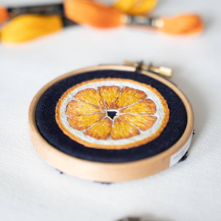 A close up shot of a finished orange slice embroidery design on navy fabric with thread in the background.