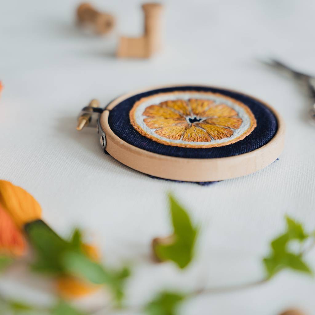 An Angled photo of a finished orange slice needle painting design on navy fabric with leaves in the foreground.