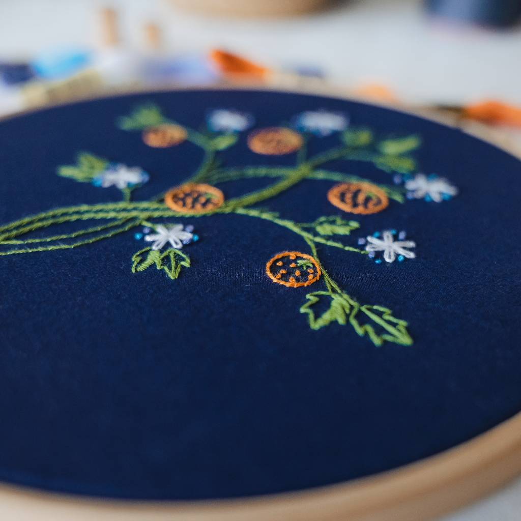 A closeup angled photo of a finished orange tree embroidery design on navy fabric, made using this orange tree embroidery kit product.