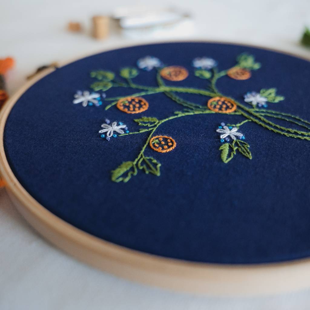 An angled photo from the left side of a finished orange tree embroidery design on navy fabric. Made using this orange tree embroidery kit product.