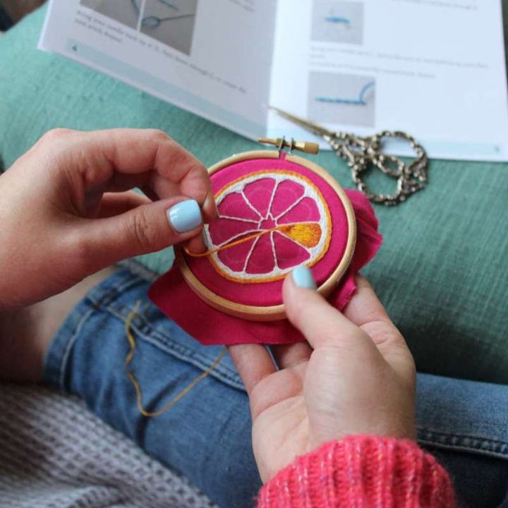 An orange embroidery design being completed on pink fabric with scissors in background