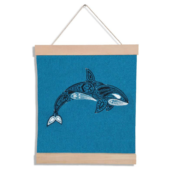 A wooden banner holding a teal square of fabric, set against a white background. The fabric is embroidered with a paisley style orca design.