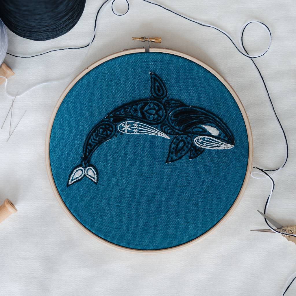 A finished orca embroidery design on organic teal fabric with thread surrounding it. Made using this Orca embroidery kit product.