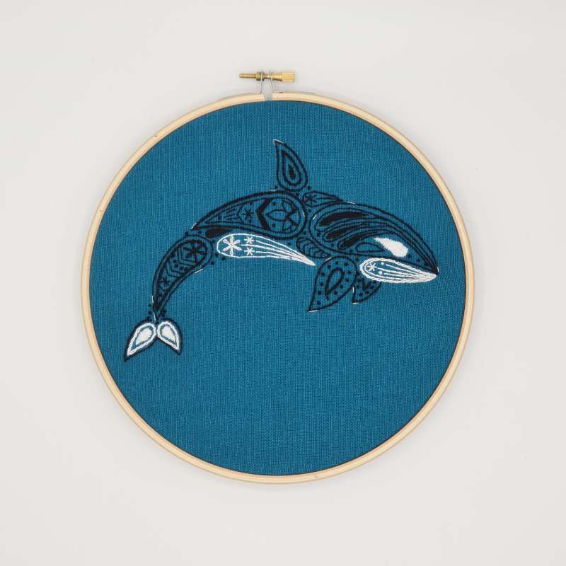 A black and white orca embroidered on teal fabric