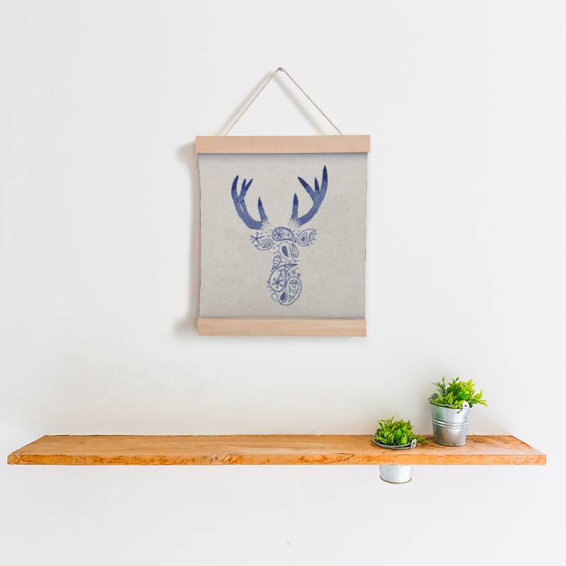 A wooden banner holding some cream fabric, displayed an embroidered paisley deer design in blue and purple thread.