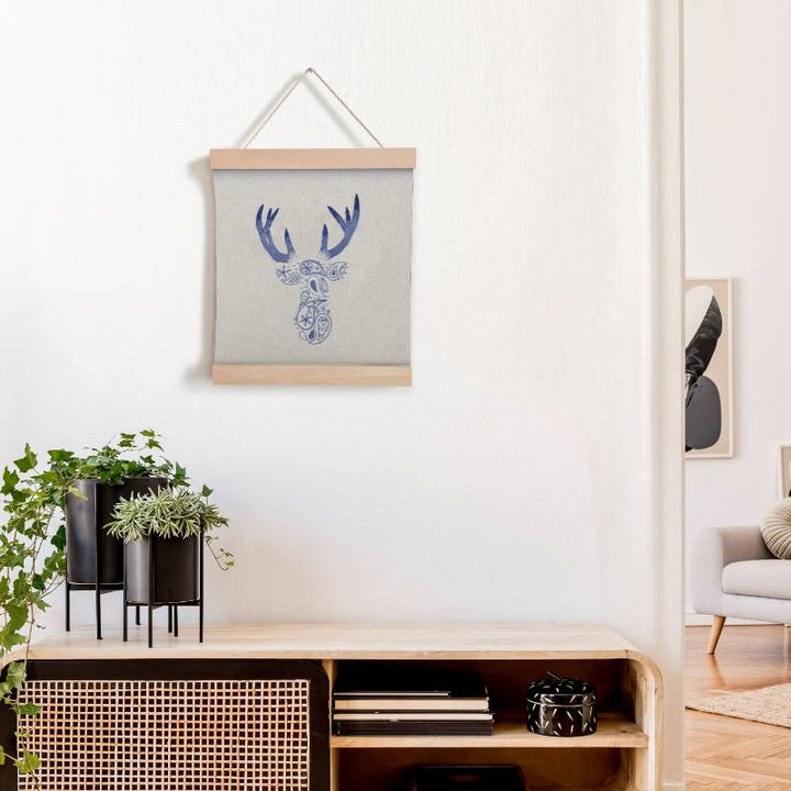 A wooden banner holding some cream fabric, displayed an embroidered paisley deer design in blue and purple thread.