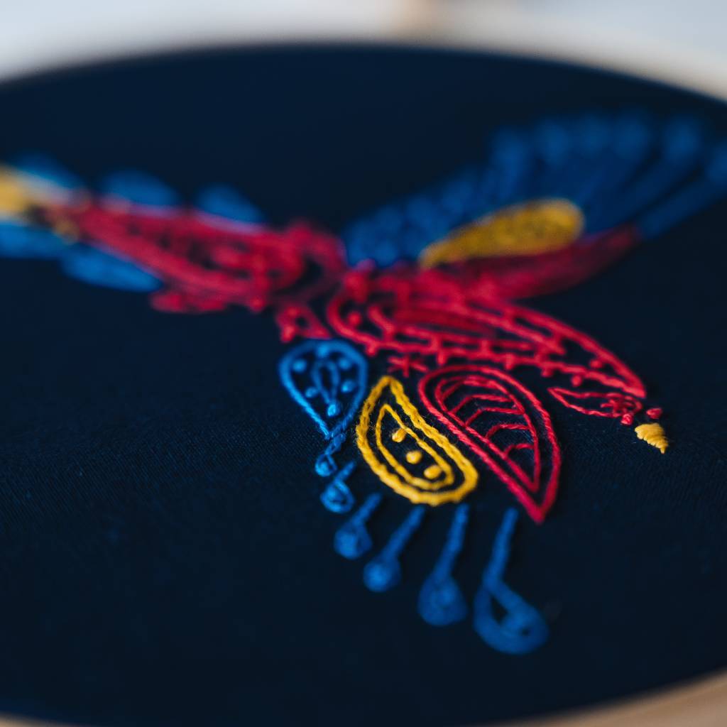 A finished parrot embroidery design shown from an angle on navy fabric, made using this parrot embroidery kit product.