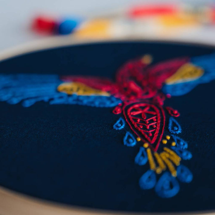 An angled photo showing a finished parrot embroidery design from the tail on navy fabric, made using this parrot embroidery kit product.