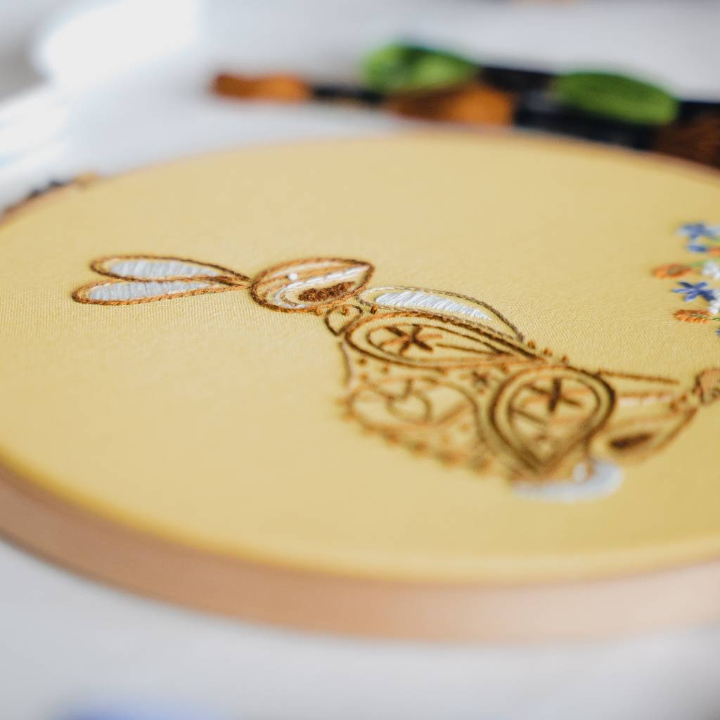 An angled closeup photo of a finished rabbit embroidery design on yellow fabric, with thread in the background. Made using this rabbit embroidery kit product.