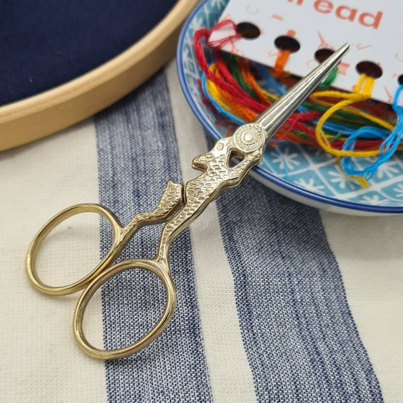 A pair of rabbit embroidery scissors resting on a small bowl containing colourful thread.