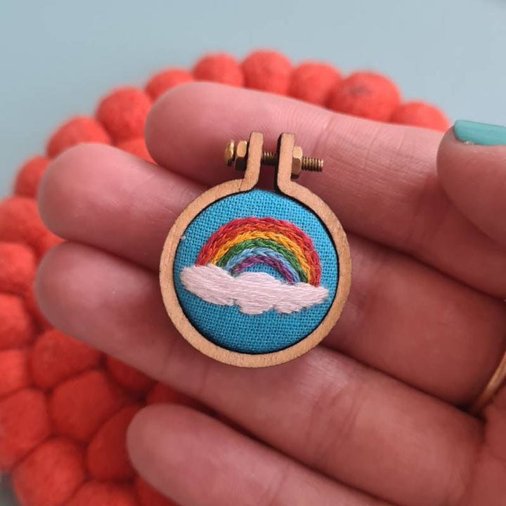 A rainbow stitched into sky blue fabric in a charm on a hand