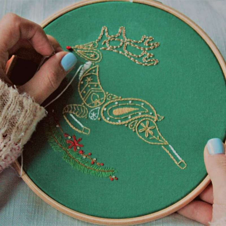 A brown and white reindeer embroidered on green fabric