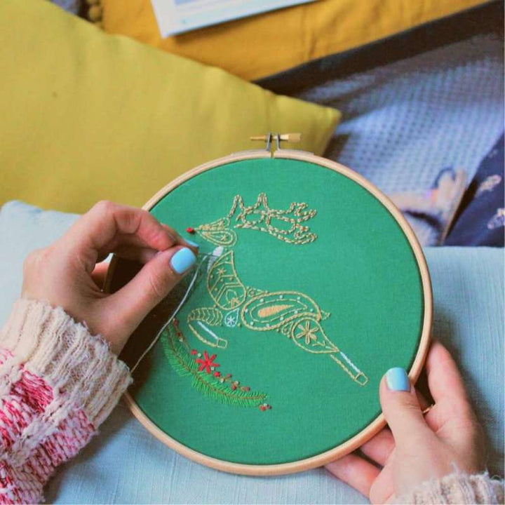 Someone embroidering a brown and white paisley reindeer onto green fabric