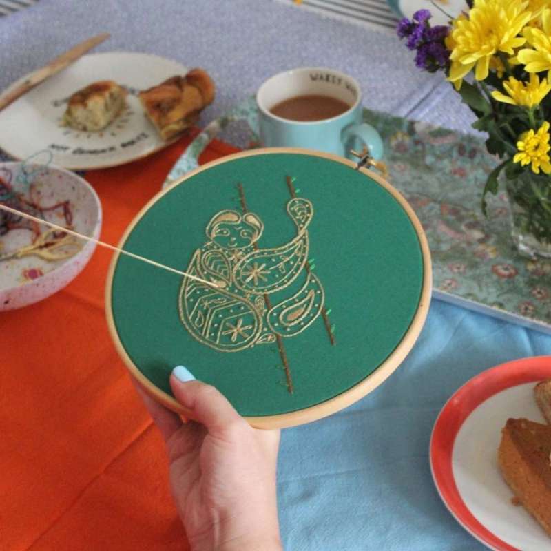 Paisley sloth embroidery kit being completed with table, flowers and cakes and tea in the background