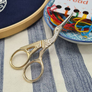 A pair of stork embroidery scissors resting on a small bowl containing colourful thread.