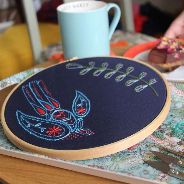 Angled photo of a blue and red swallow next to a green leafy embroidered branch