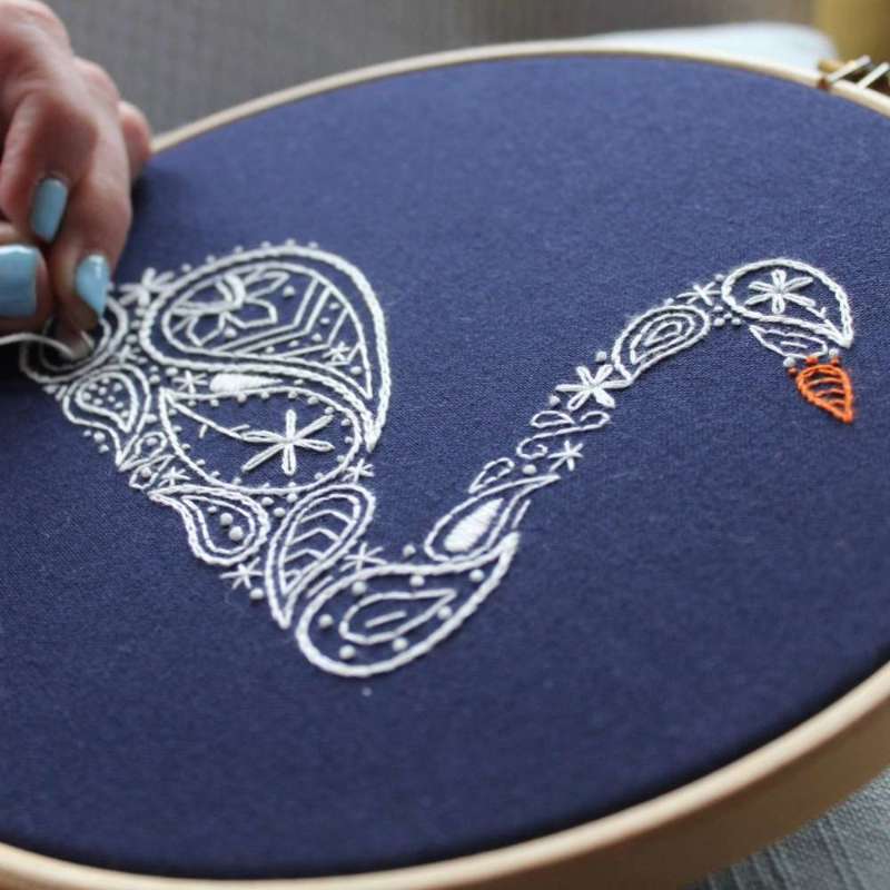Paisley inspired white swan embroidery kit with orange beak on navy fabric being sewn