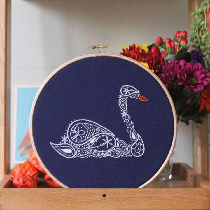 White swan embroidery kit on navy fabric in a wooden hoop on a shelf