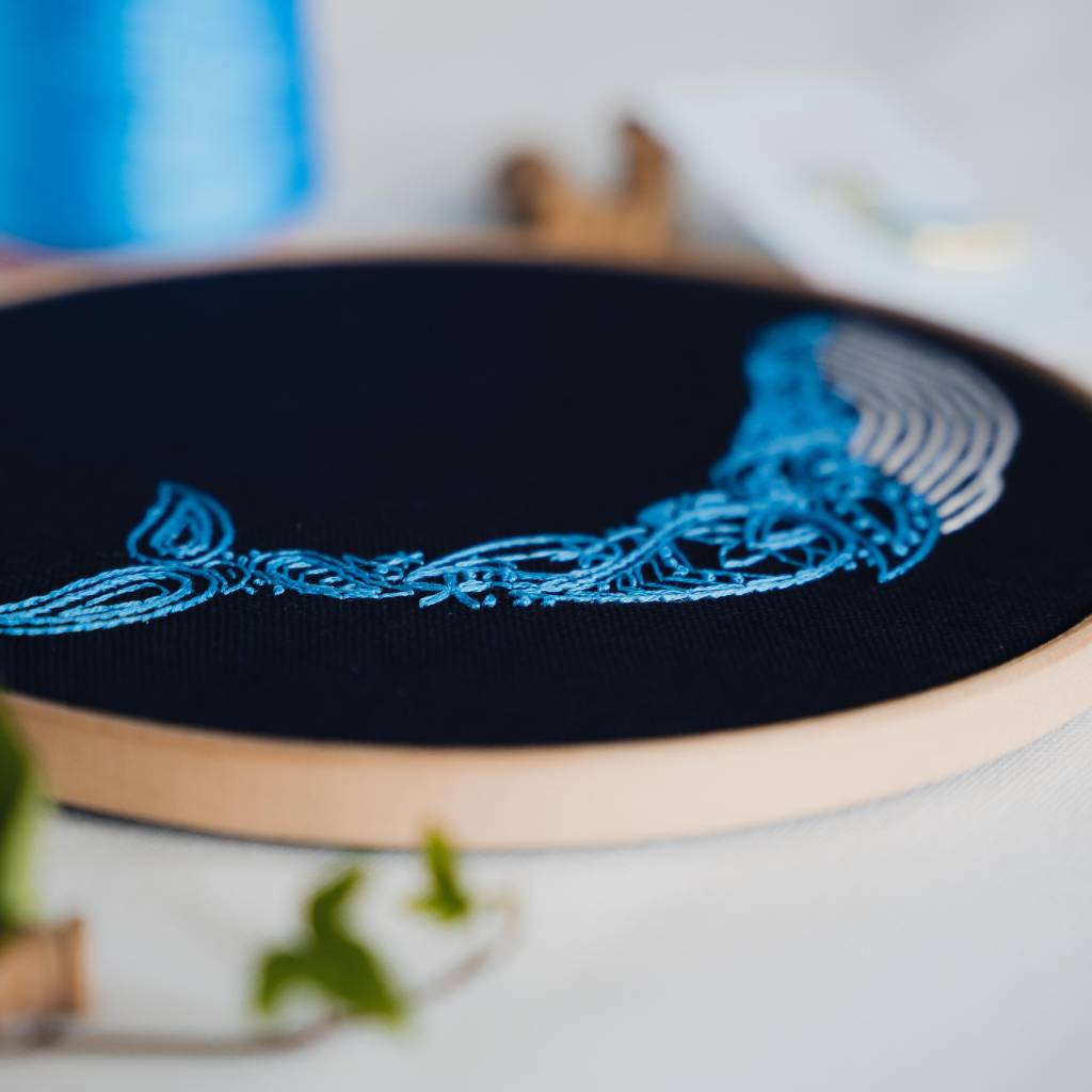 An angled photo of a whale embroidery design on navy fabric, made using this whale embroidery kit product.