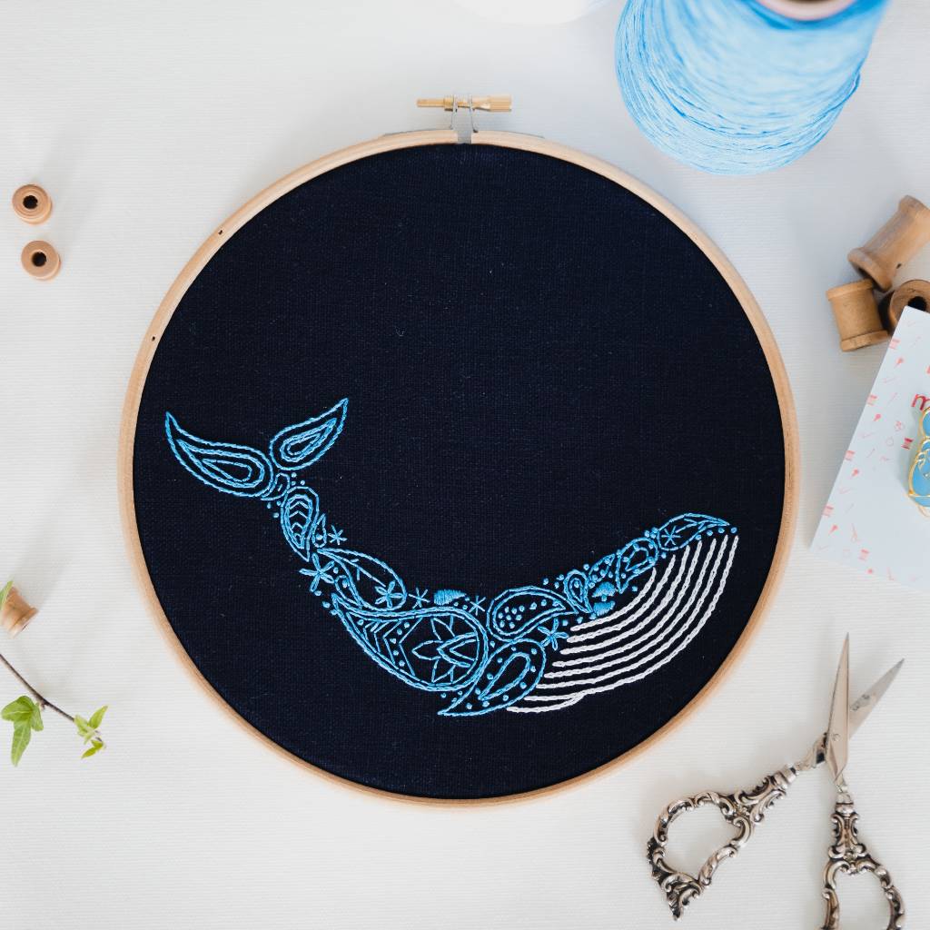 A finished whale embroidery design on navy fabric, with thread and spools above and scissors below. Made using this whale embroidery kit product.