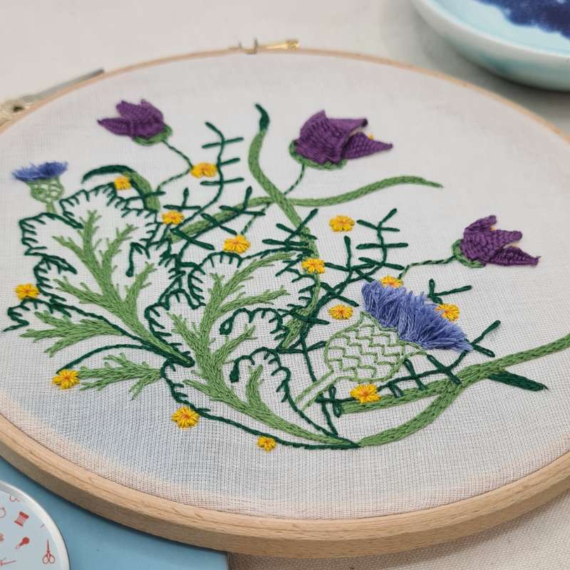 Close up angled shot of botanicals embroidery on purple fabric
