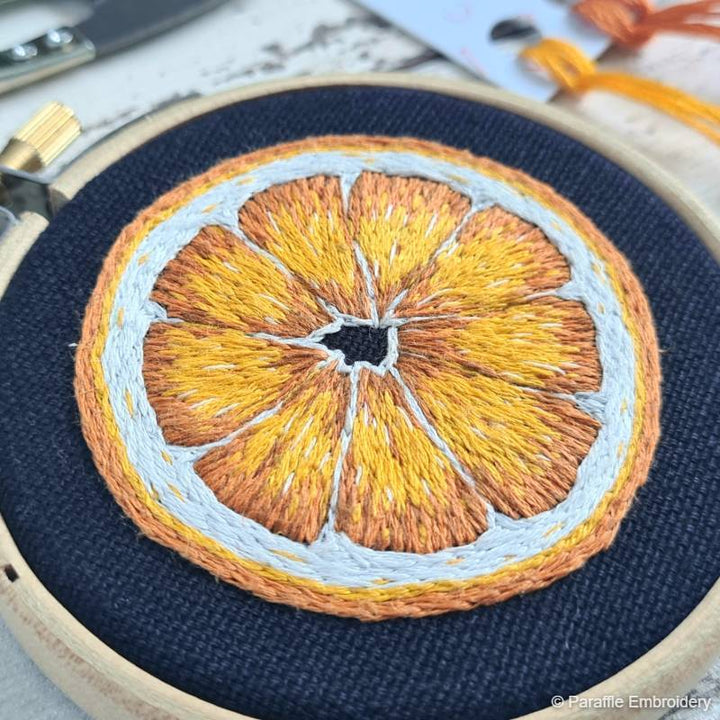 Detail picture of orange needle painting embroidery on navy fabric in wooden hoop